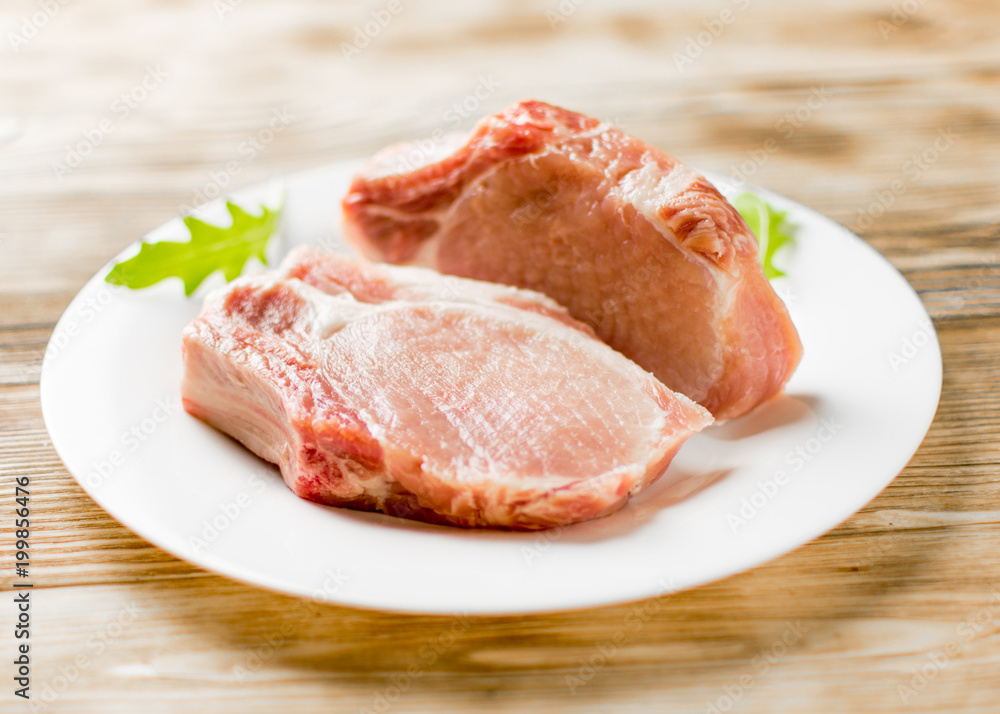 Raw pork brisket, ribs on a white plate on a wooden background. Raw pork brisket, ribs on a white plate on a wooden background.