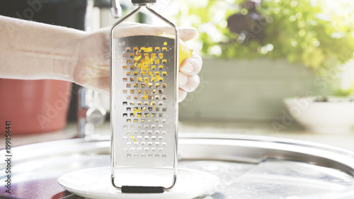 A young woman is holding a grater and peel a lemon zest into a small white plate. photo