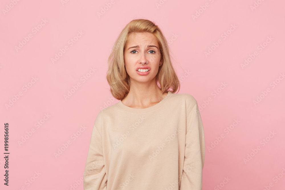 Dissatisfied female model frowns face, has disgusting expression, expresses non compliance, irritated with somebody, wears yellow sweater. Negative emotion concept. Isolated over pink background Dissatisfied female model frowns face, has disgusting expression, expresses non compliance, irritated with somebody, wears yellow sweater. Negative emotion concept. Isolated over pink background
