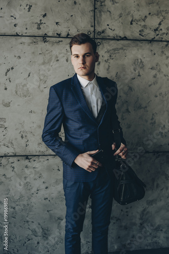 Portrait of young businessman holding a smartphone in one hand and a leather bag on his shoulder.