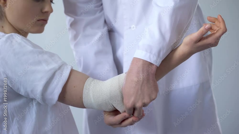 Doctor bandaging injured patient hand, first aid for sprain in trauma clinic Doctor bandaging injured patient hand, first aid for sprain in trauma clinic