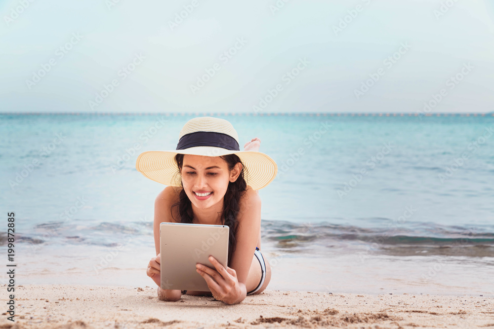 Young woman using tablet computer on the beach.