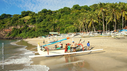 Fischerboot an weißem Sandstrand Virgin Beach in Ost-Bali wird angelandet vor grünen Palmen