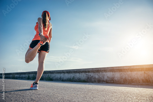 An asian woman athletic is jogging on the concrete road  she is warming her body and tideten her tying her shoes tightly fitting before workout.