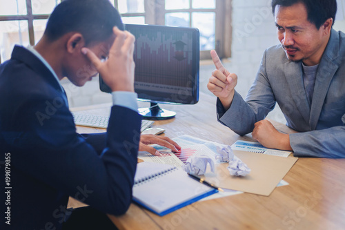 Businessman as boss blaming and admonish his employee for business mistake at desk in office
