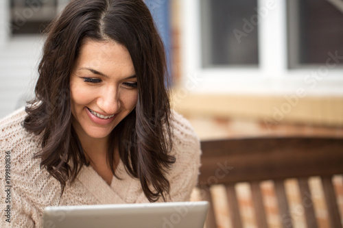 Free Download Happy woman sitting outside reading on a tablet. - GFXLoad