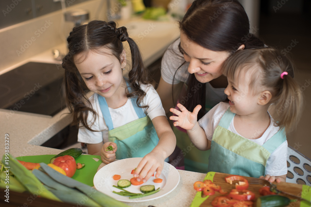 Happy family mom and kids preparing vegetables together at home in the kitchen Happy family mom and kids preparing vegetables together at home in the kitchen