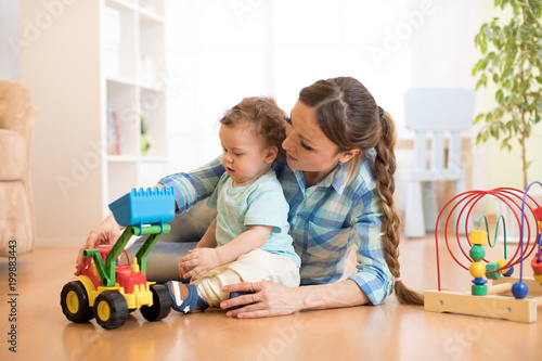 Little baby boy and mom playing on the floor with tractor toy