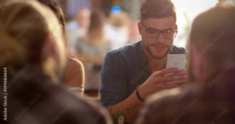 Young hipster man using mobile phone in cafe with friends