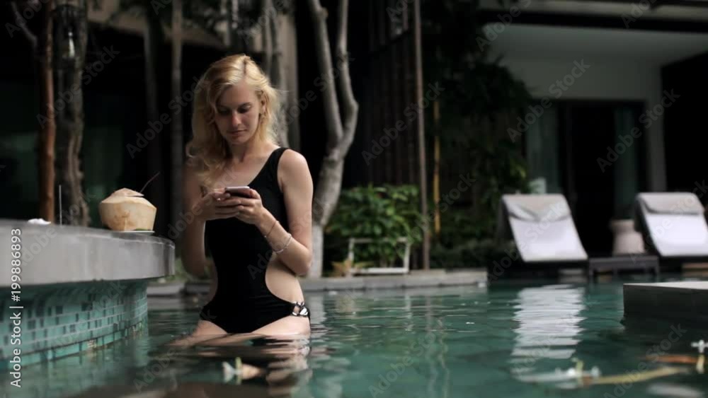 beautiful woman with phone sitting in pool at the bar beautiful woman with phone sitting in pool at the bar