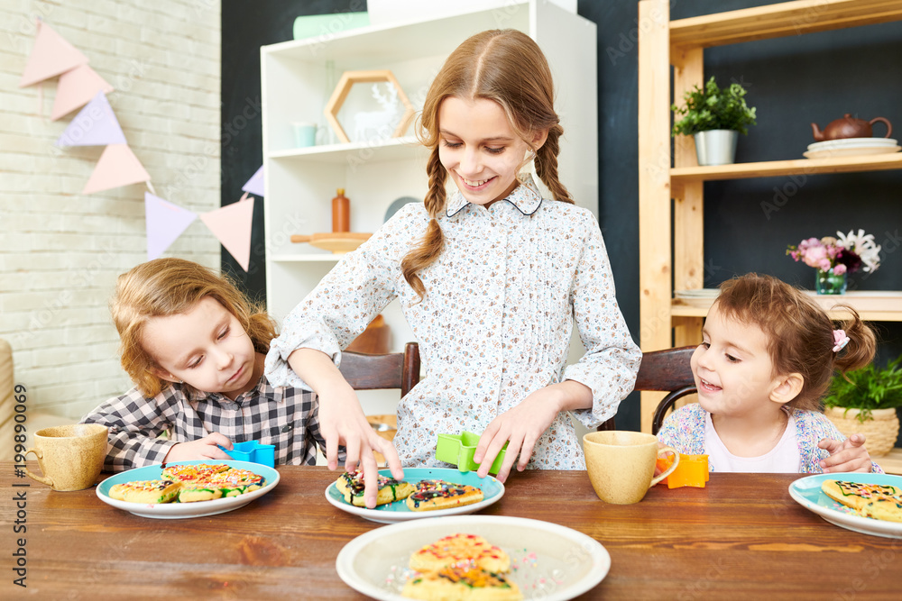 Smiling little girl with two braids standing at wooden table of spacious dining room and playing with homemade waffles and cookie cutter, her sisters keeping eye on her Smiling little girl with two braids standing at wooden table of spacious dining room and playing with homemade waffles and cookie cutter, her sisters keeping eye on her