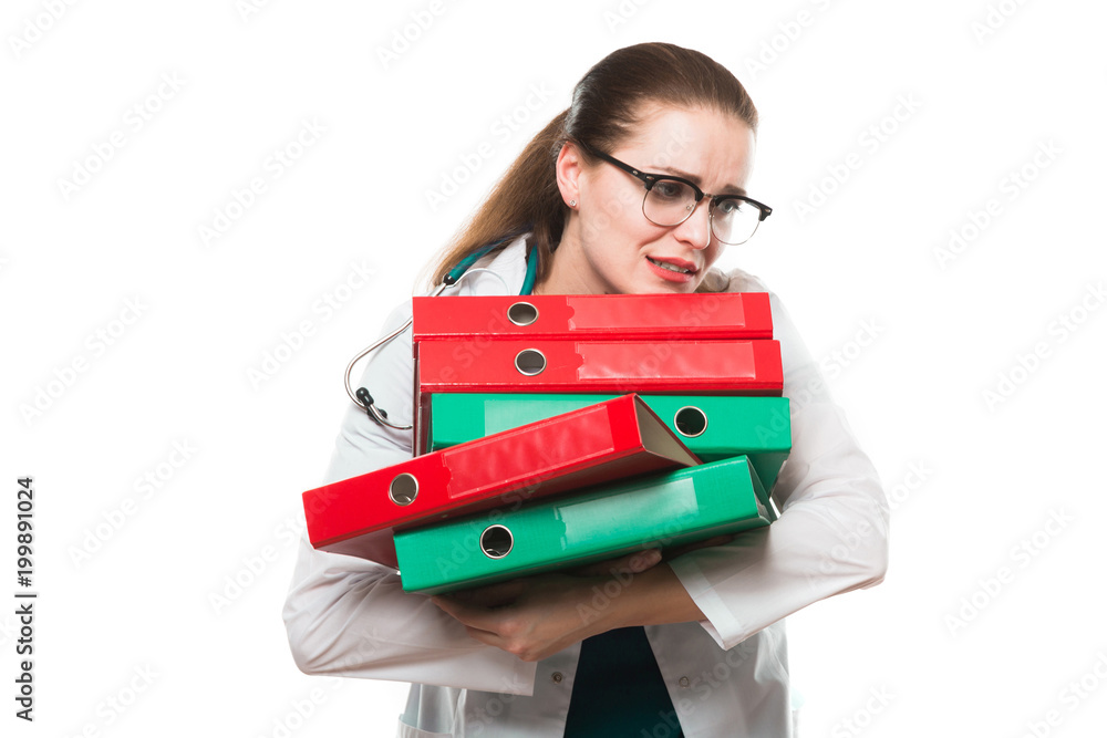 Attractive caucasian brunette sad female doctor standing in office with binders in her hands on white background Attractive caucasian brunette sad female doctor standing in office with binders in her hands on white background