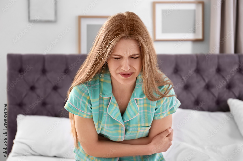Young woman suffering from stomach ache in bedroom Young woman suffering from stomach ache in bedroom
