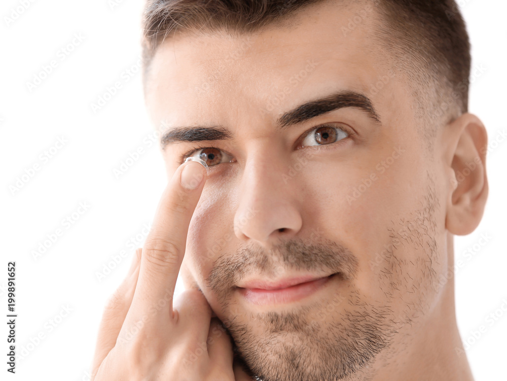 Obraz premium Young man putting contact lens in his eye on light background