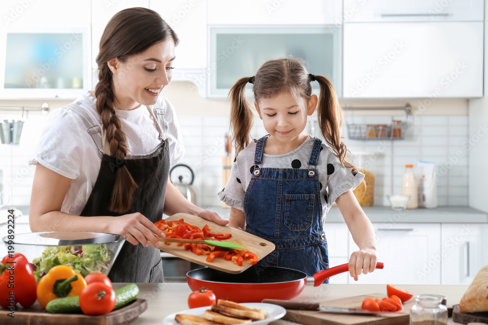 Young nanny with cute little girl cooking together in kitchen