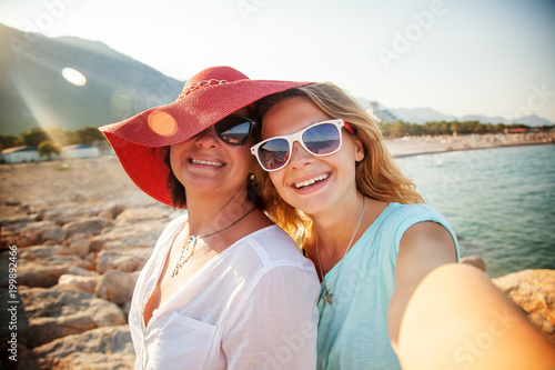 Sticker An attractive middle-aged woman with her adult daughter doing selfie on the beac