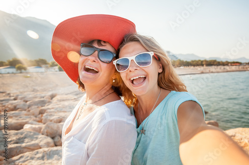 An attractive middle-aged woman with her adult daughter doing selfie on the beach, vacation and travel, cruise and sea