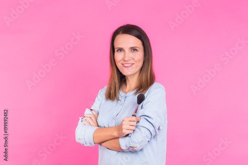 Portrait of makeup artist with brushes in hand on a pink background.