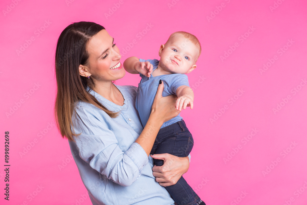 family, motherhood, parenting, people and child care concept - happy mother holds adorable baby over pink background family, motherhood, parenting, people and child care concept - happy mother holds adorable baby over pink background