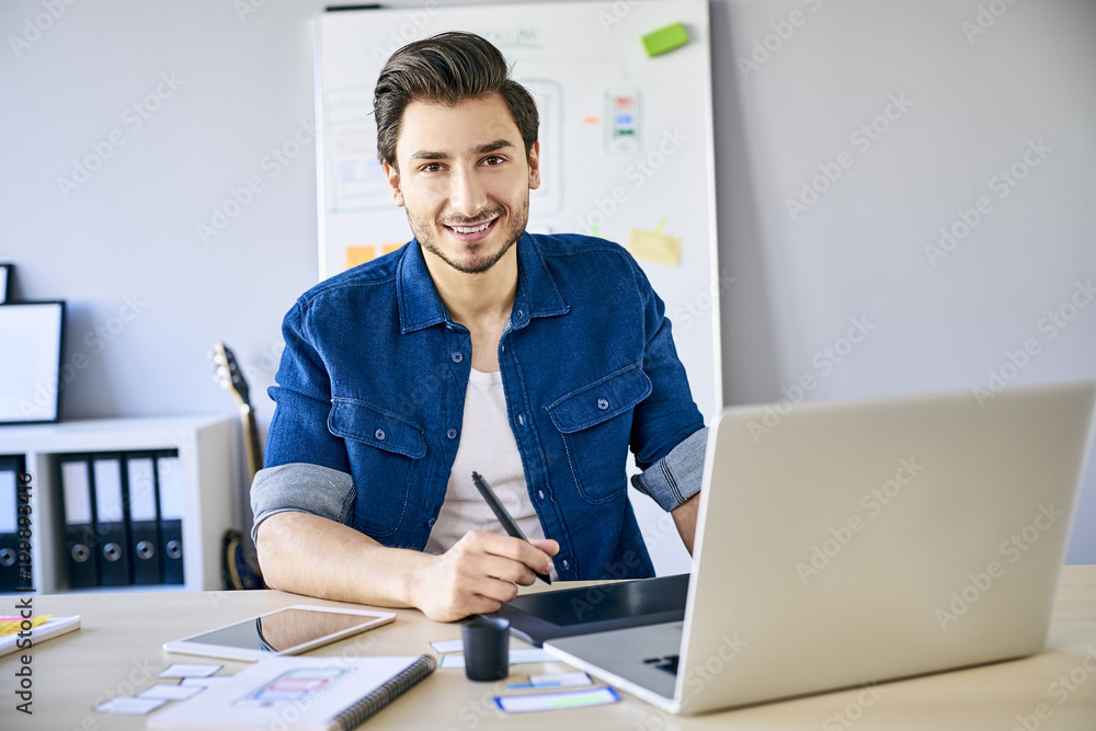 Young designer looking at camera while working with graphics tablet and laptop Young designer looking at camera while working with graphics tablet and laptop