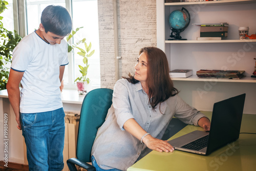 A middle-aged woman checks a teen's son's laptop, banned materials and computer security, uncompleted homework