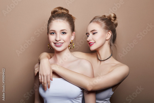 Two sexy young blonde hair girls hugging, earrings in ears jewelry on neck and, beautiful eyes. Summer skin care eye shadow, fashion natural skin care, face skin art, body beauty nature, spring makeup