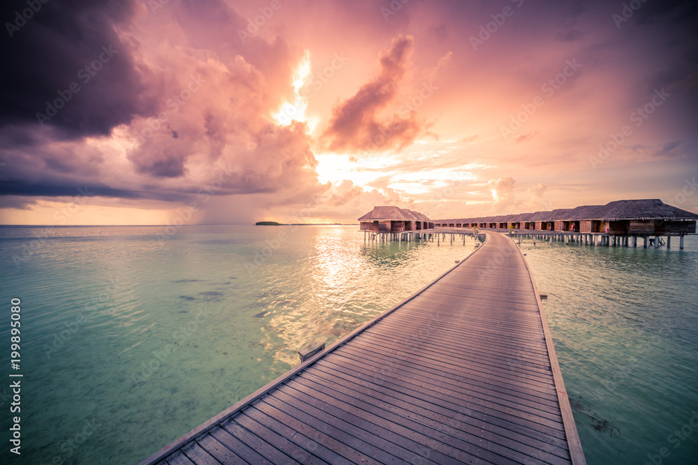 Maldives sunset beach. Sky and stormy clouds with luxury water villas and wooden pier