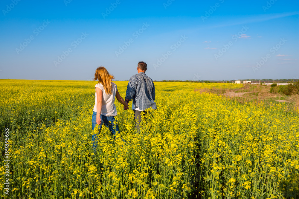 Romantic couple is walking through the field of yellow flowers
