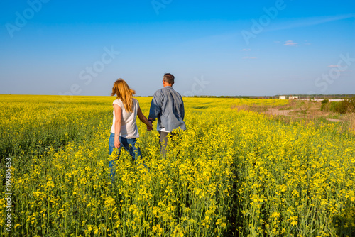 Romantic couple is walking through the field of yellow flowers © sanechka