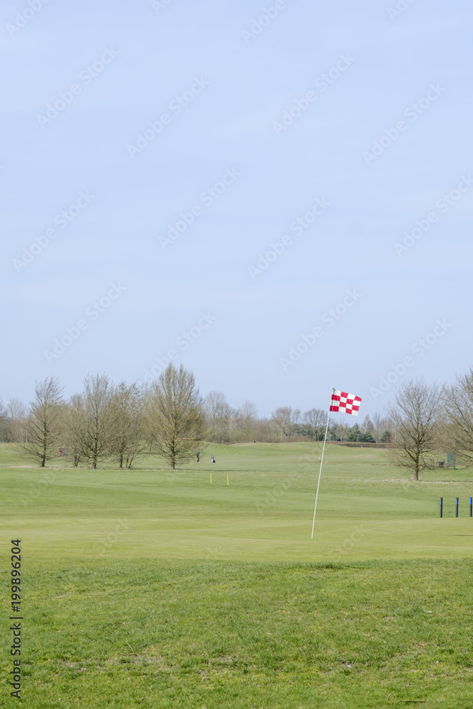 Obraz premium A red and white checkered golf course flagstick on a putting green.