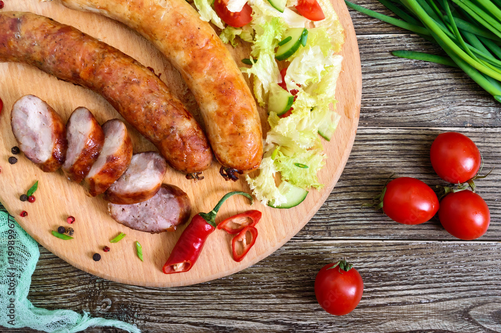 Juicy home made sausage with a light spring salad of fresh vegetables on a wooden tray on the table. A traditional Easter dish. Top view. Juicy home made sausage with a light spring salad of fresh vegetables on a wooden tray on the table. A traditional Easter dish. Top view.