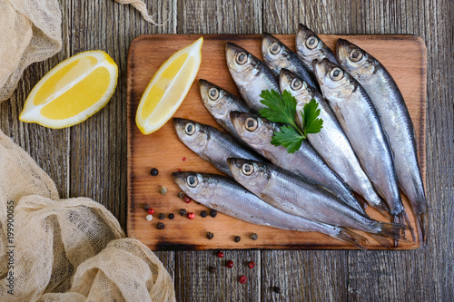 A small salted hamsa (sprat) with spices, lemon on a wooden background. Top view. photo