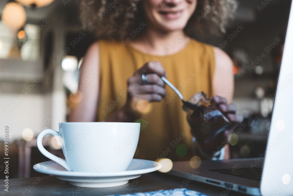 Handsome woman in city cafe, with cup of coffee and latop, adding sugar into her drink Handsome woman in city cafe, with cup of coffee and latop, adding sugar into her drink