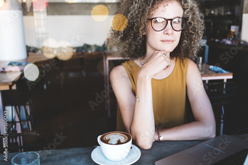 Portrait of handsome curly woman in city cafe. With laptop and cup of coffee