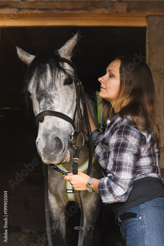 girl in plaid shirt with a horse in a stable