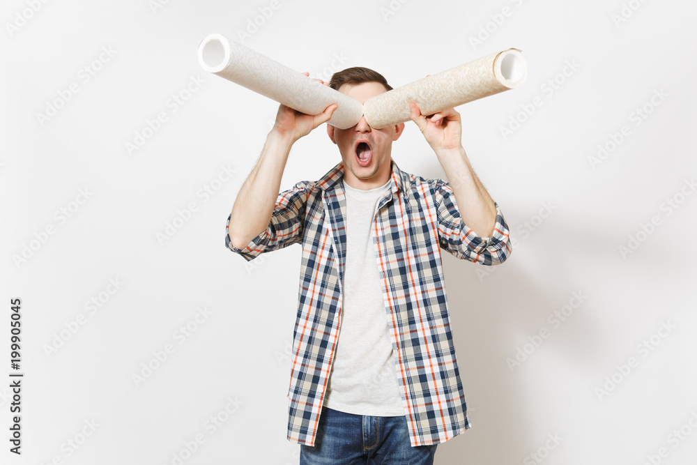Young fun handsome man in casual clothes looks through wallpaper roll as with binoculars or spyglass isolated on white background. Instruments for renovation apartment room. Repair home concept. Young fun handsome man in casual clothes looks through wallpaper roll as with binoculars or spyglass isolated on white background. Instruments for renovation apartment room. Repair home concept.