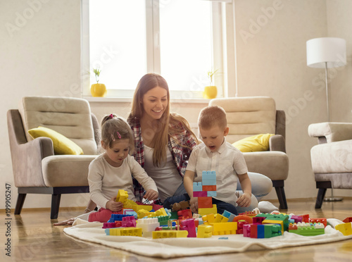 Mother with children playing together with block toys in living room