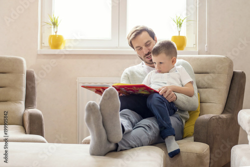 Father and son reading book and having fun while spending time together at home