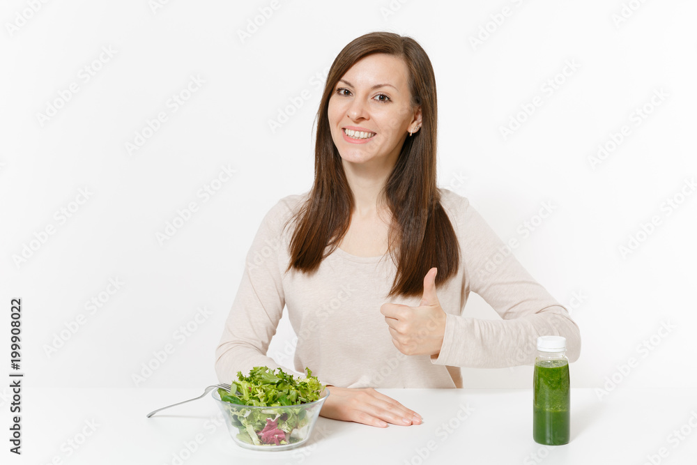 Young woman sitting at table with green detox smoothies, salad in glass bowl isolated on white background. Proper nutrition, vegetarian food, healthy lifestyle, dieting concept. Area with copy space. Young woman sitting at table with green detox smoothies, salad in glass bowl isolated on white background. Proper nutrition, vegetarian food, healthy lifestyle, dieting concept. Area with copy space.