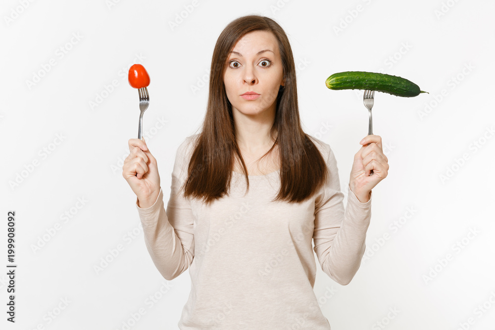 Irritated vegan woman holds green cucumber, red tomato on fork isolated on white background. Proper nutrition, vegetarian food, healthy lifestyle, vegetable concept. Advertising area with copy space. Irritated vegan woman holds green cucumber, red tomato on fork isolated on white background. Proper nutrition, vegetarian food, healthy lifestyle, vegetable concept. Advertising area with copy space.