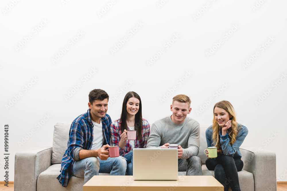 The four people with cups sit near laptop on the white wall background The four people with cups sit near laptop on the white wall background