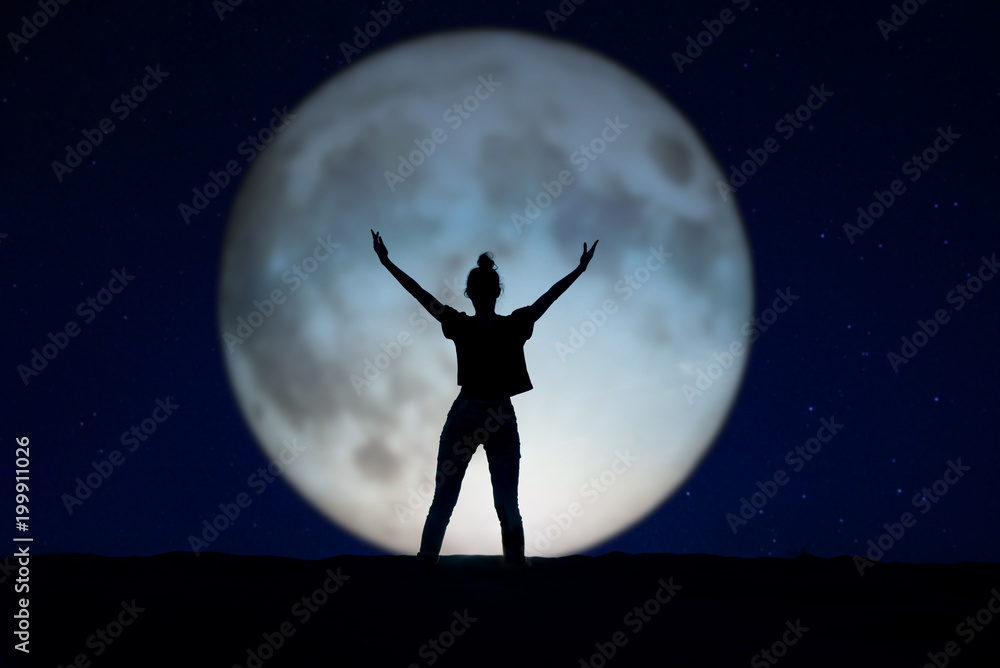 Silhouette of a woman standing in the night with the arms up, giant moon in the background Silhouette of a woman standing in the night with the arms up, giant moon in the background