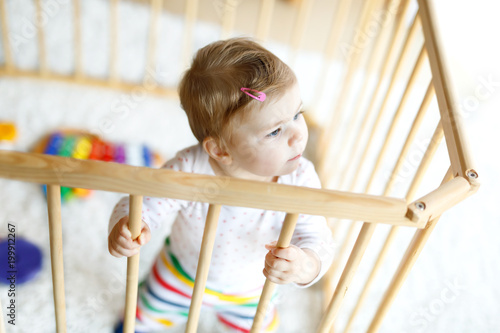 Beautiful little baby girl standing inside playpen. Cute adorable child playing with colorful toy photo