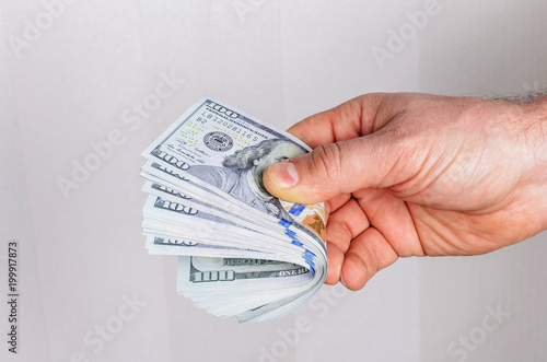 the man's hand holds a stack of dollars in dollars worth a hundred dollars on a light background