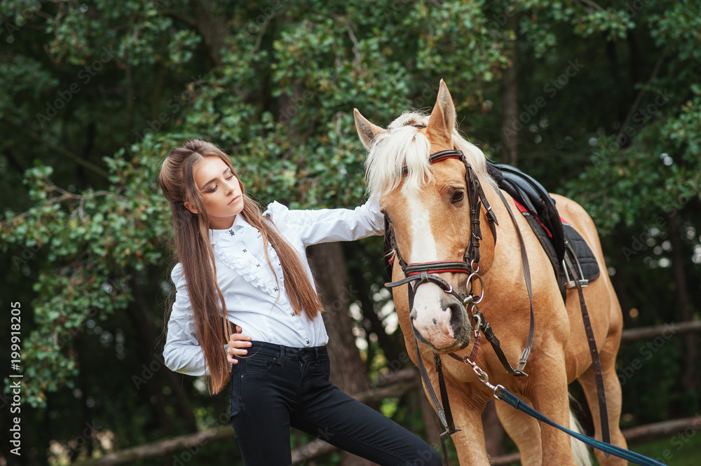 Fototapeta premium portrait beautiful young girl in white shirt and black pants with beauty long hair next horse in forest. Fashionable elegance woman posing near animal. Beauty Lifestyle Fashion People Animals concepts