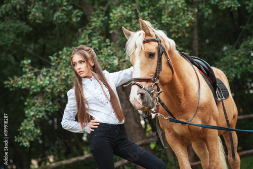 portrait beautiful young girl in white shirt and black pants with beauty long hair next horse in forest. Fashionable elegance woman posing near animal. Beauty Lifestyle Fashion People Animals concepts © victoriazarubina