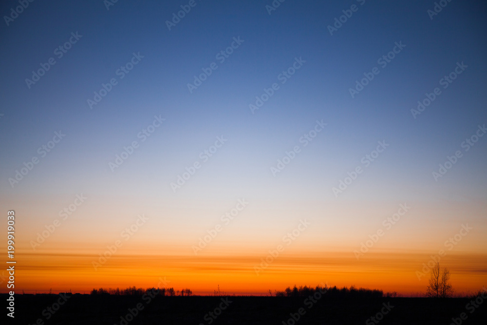 Bright red dawn with a cloudless blue sky. Silhouette of the earth and trees. Copy space for text.