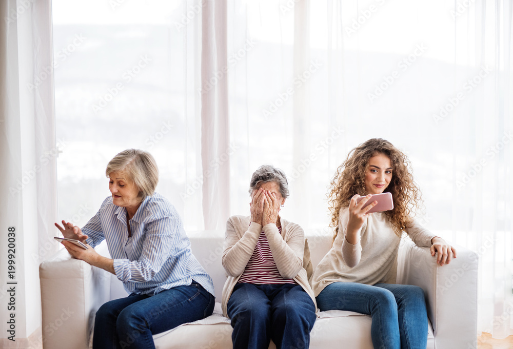 Obraz premium A teenage girl, mother and grandmother with smartphone at home.