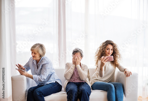 A teenage girl, mother and grandmother with smartphone at home.