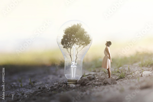 surreal image of a woman who observes intrigued a giant bulb containing a tree for renewable energy